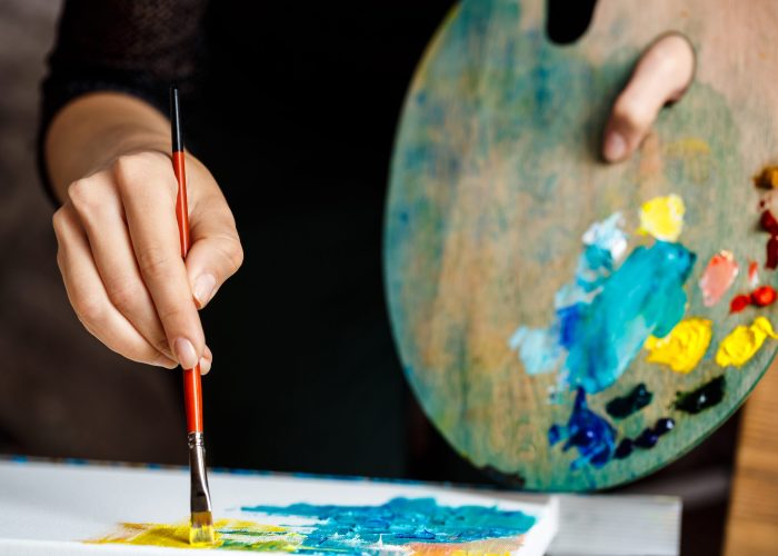 Close up photo of girl drawing with oil paints on canvas. Copy space.